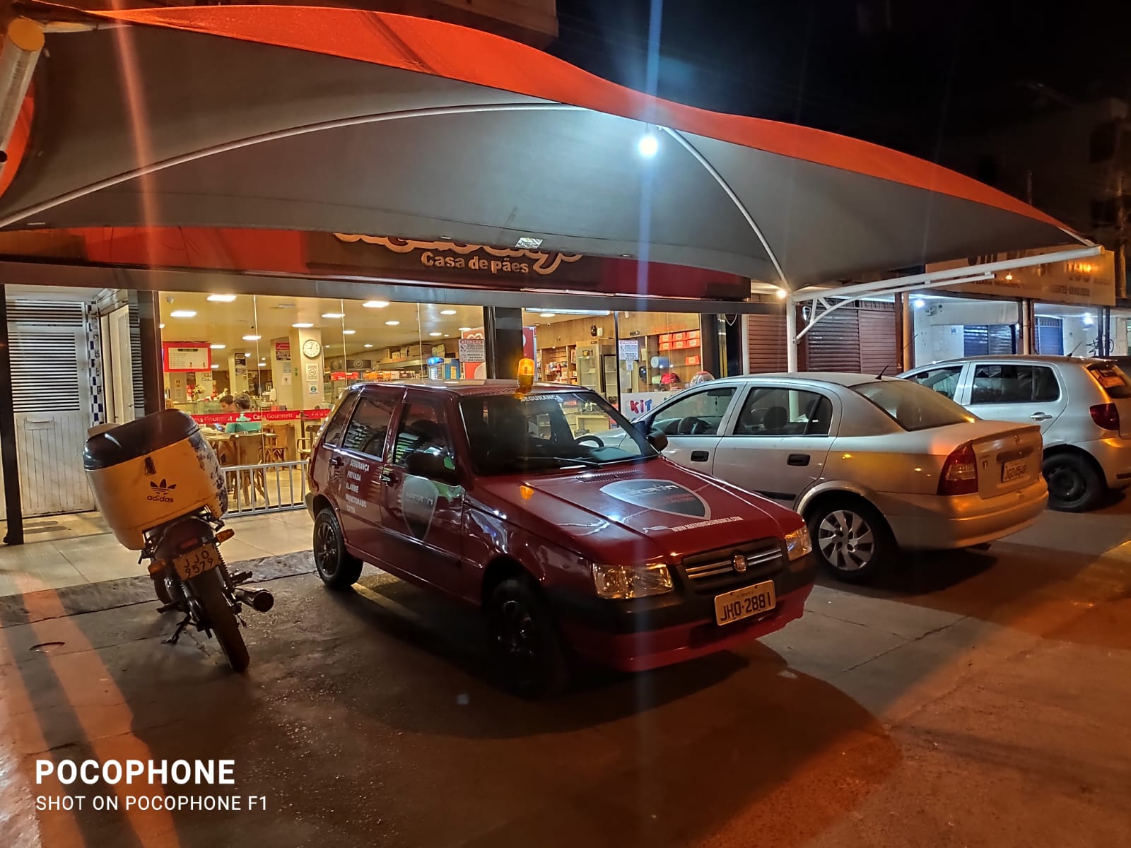 Rua noturna com carro vermelho parado próximo à padaria Casa de Pães